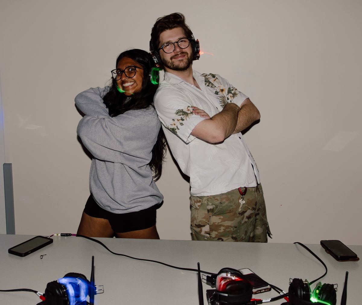 Two people wearing headsets, smiling and posing confidently beside a table with colorful headphones.