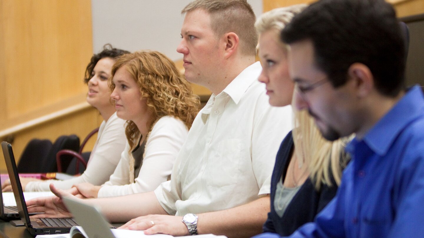 Students seated in a classroom, focused on laptops and notes.